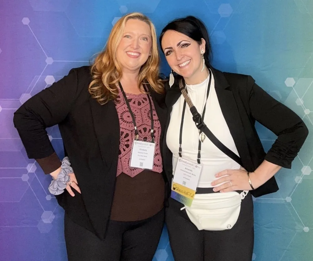 Kim Carlos, left, and Amanda Bonello, right, smiling arm in arm at a conference